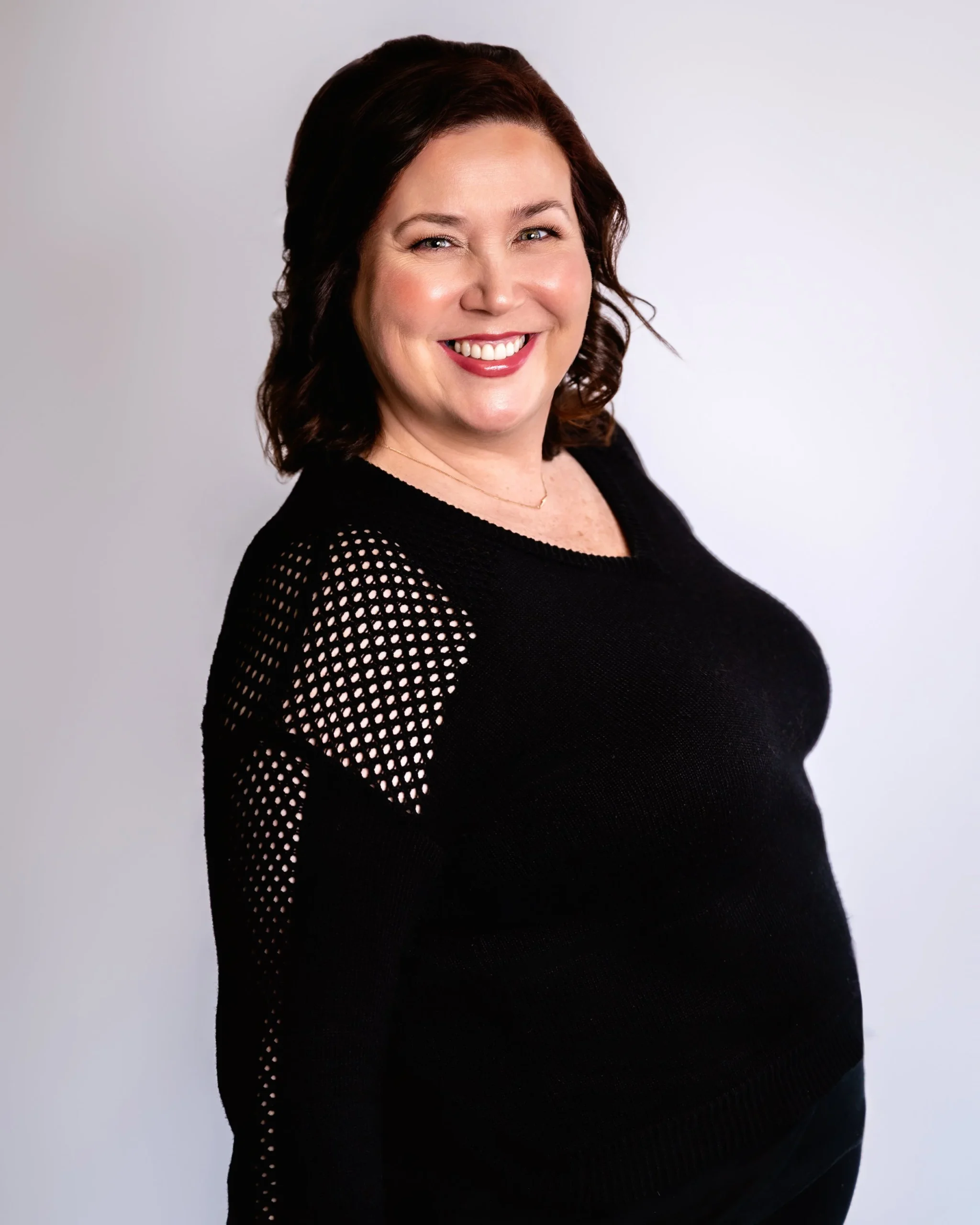 Woman smiling in a black sweater with mesh details.