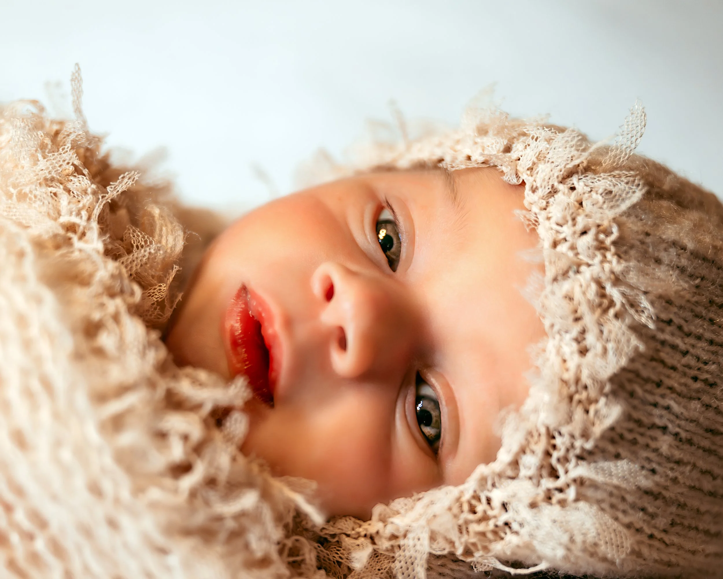 Close-up of a newborn baby wearing a lace bonnet and wrapped in a soft, textured blanket.