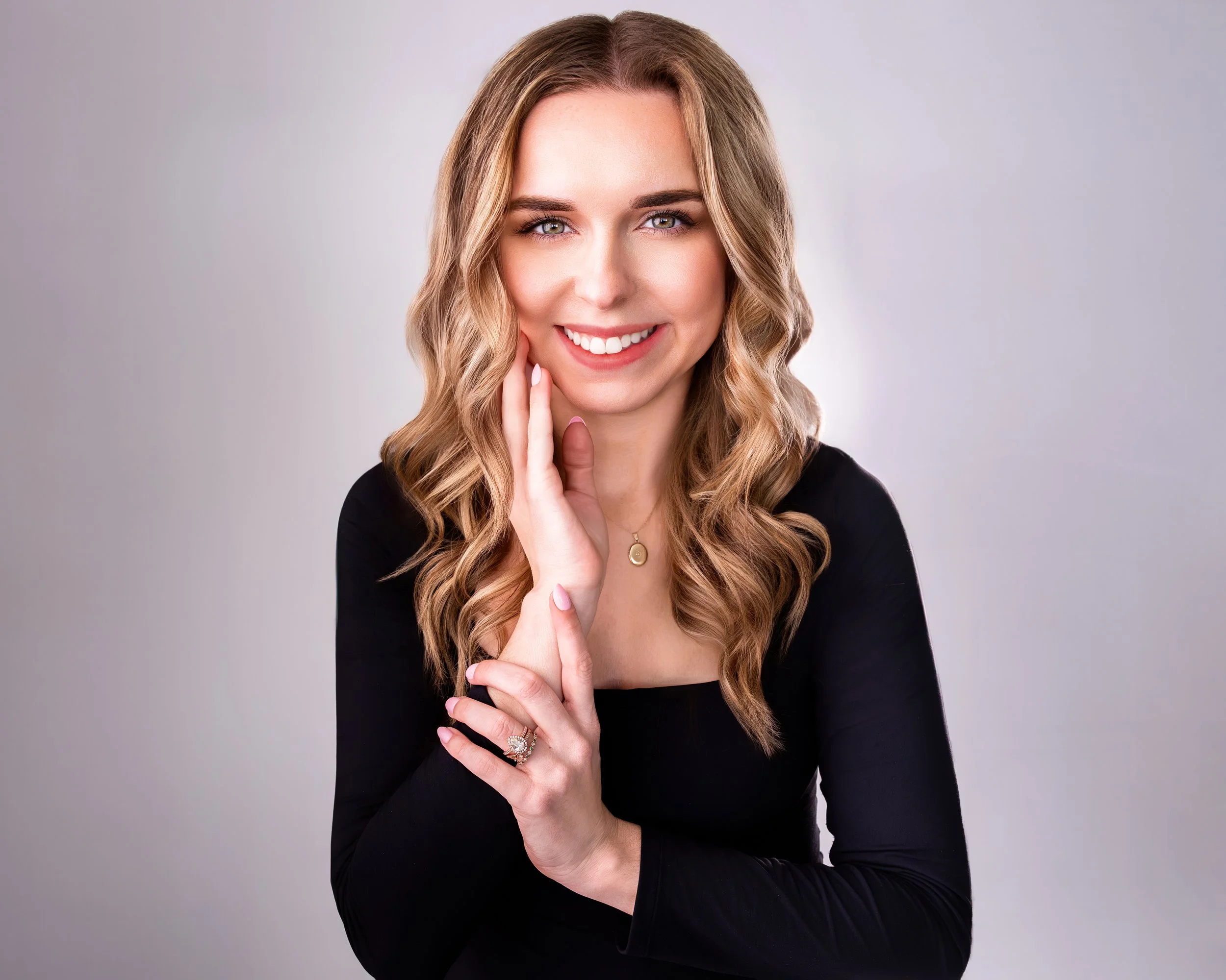 Smiling woman with curly blonde hair in black top, wearing a ring and necklace.