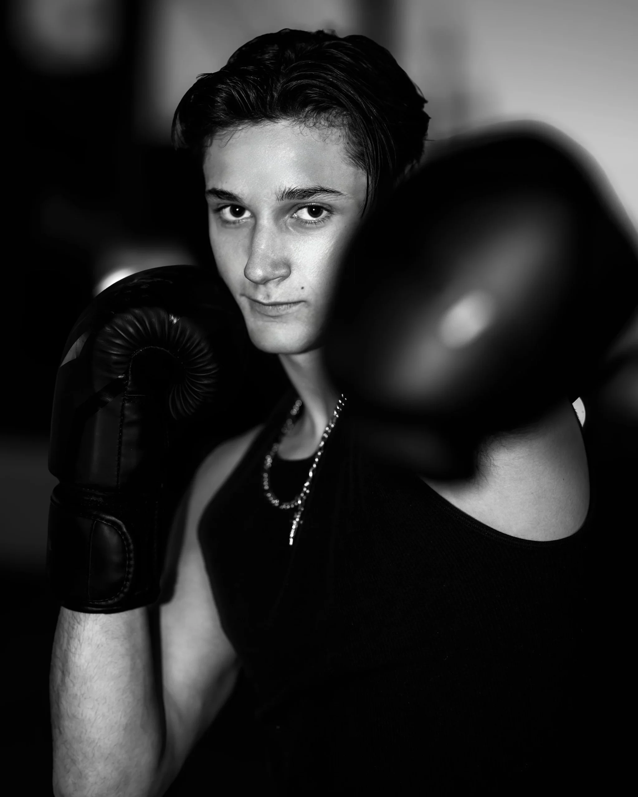 Black and white photo of a person wearing boxing gloves, looking directly at the camera.