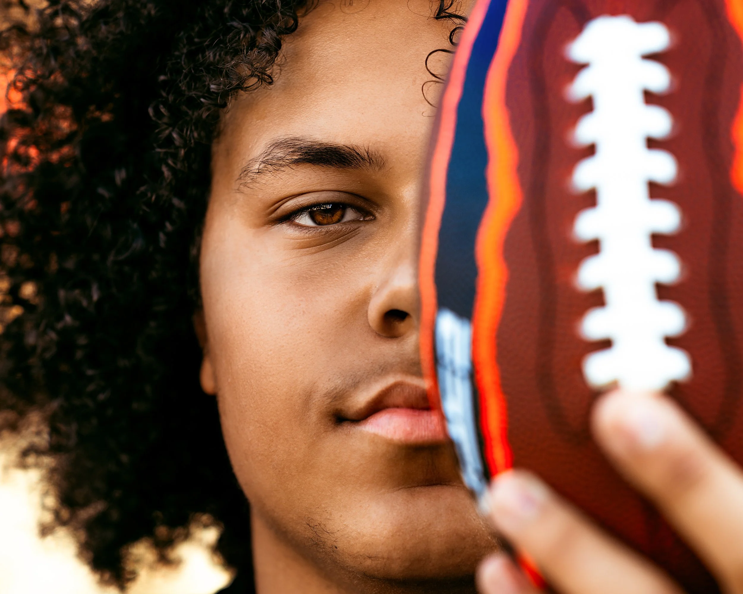 Man looking into camera while holding a football at High School Senior Photography Session with Two Wild Souls Photography