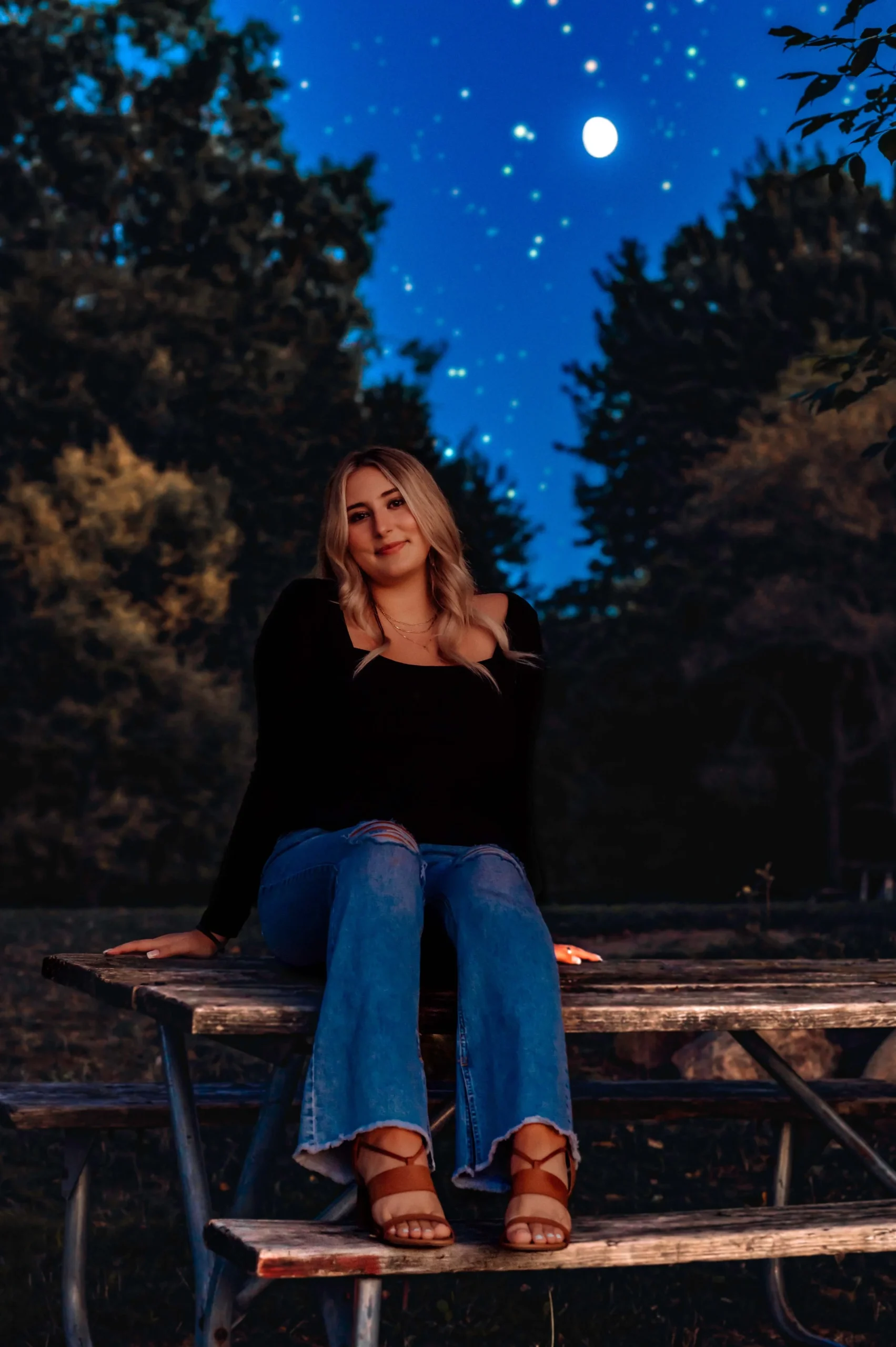 Woman sitting on picnic table at night, starry sky background