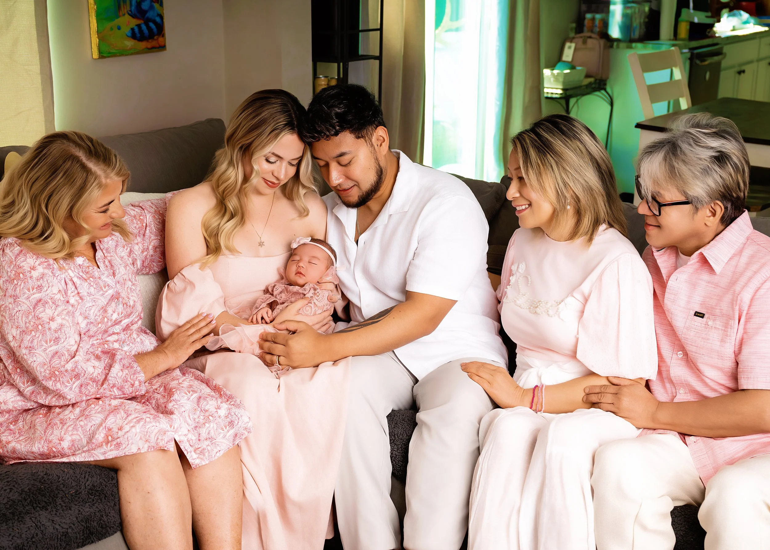 Family gathered on a couch celebrating a newborn, with five women and one man, all smiling, holding and looking at the baby.