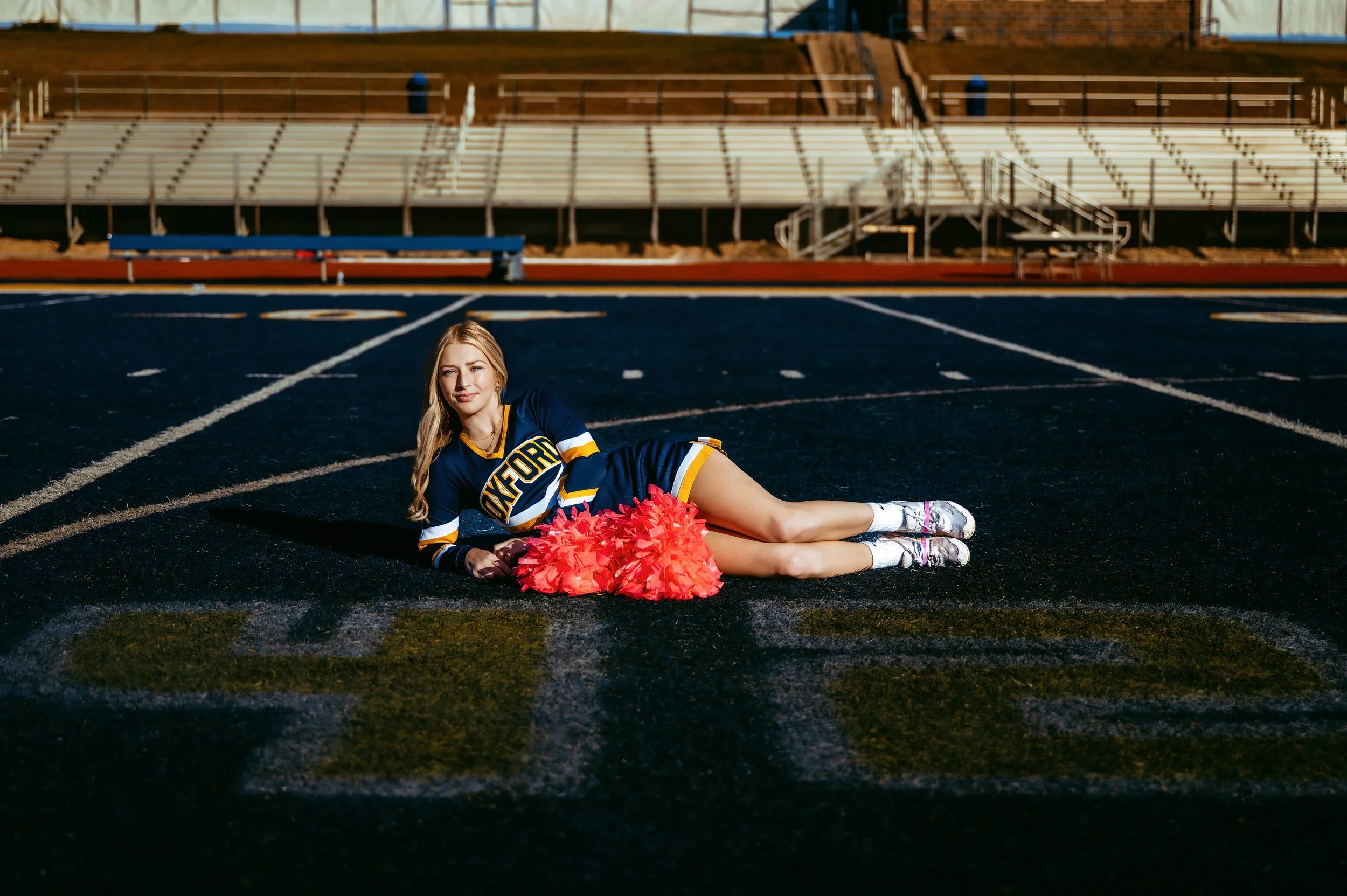 Cheerleader in uniform lying on a football field with pom-poms