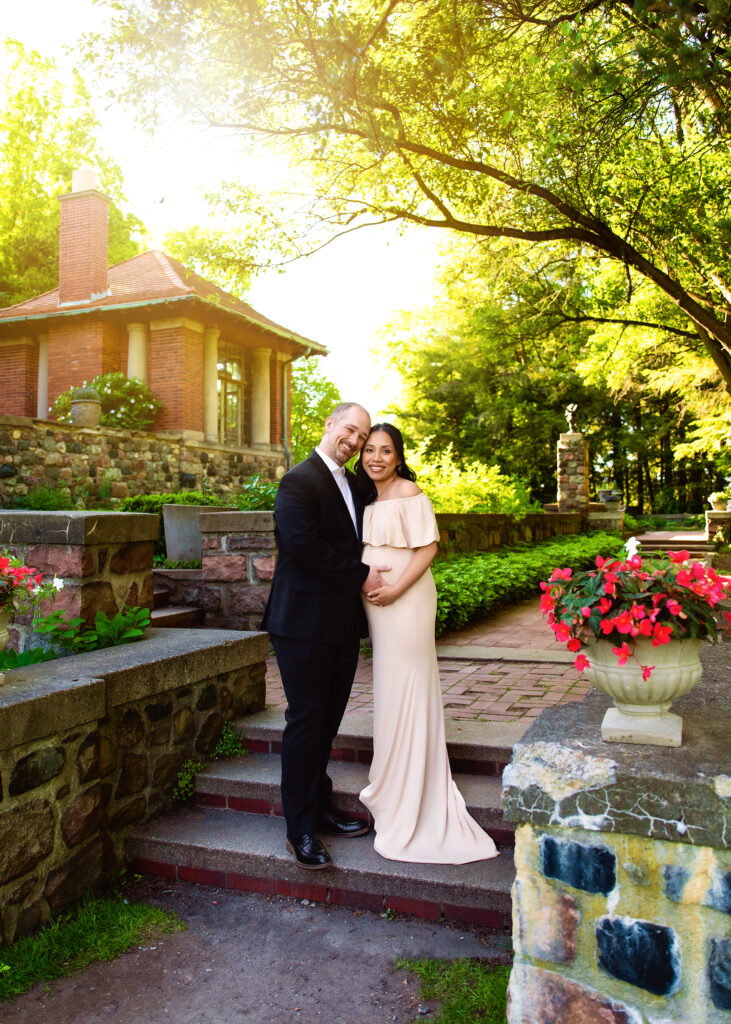 Aclipen_FINAL_5677 | Two Wild Souls Photography Pregnant woman in a pale dress and a man in a suit posing on stone steps in a sunny garden setting.
